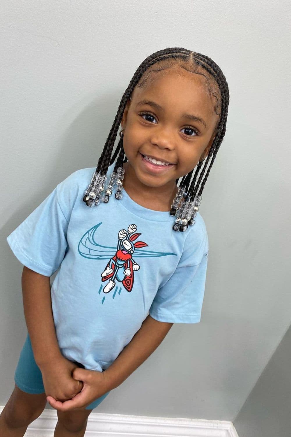 A girl wearing a blue t-shirt and shorts with beaded box braids.