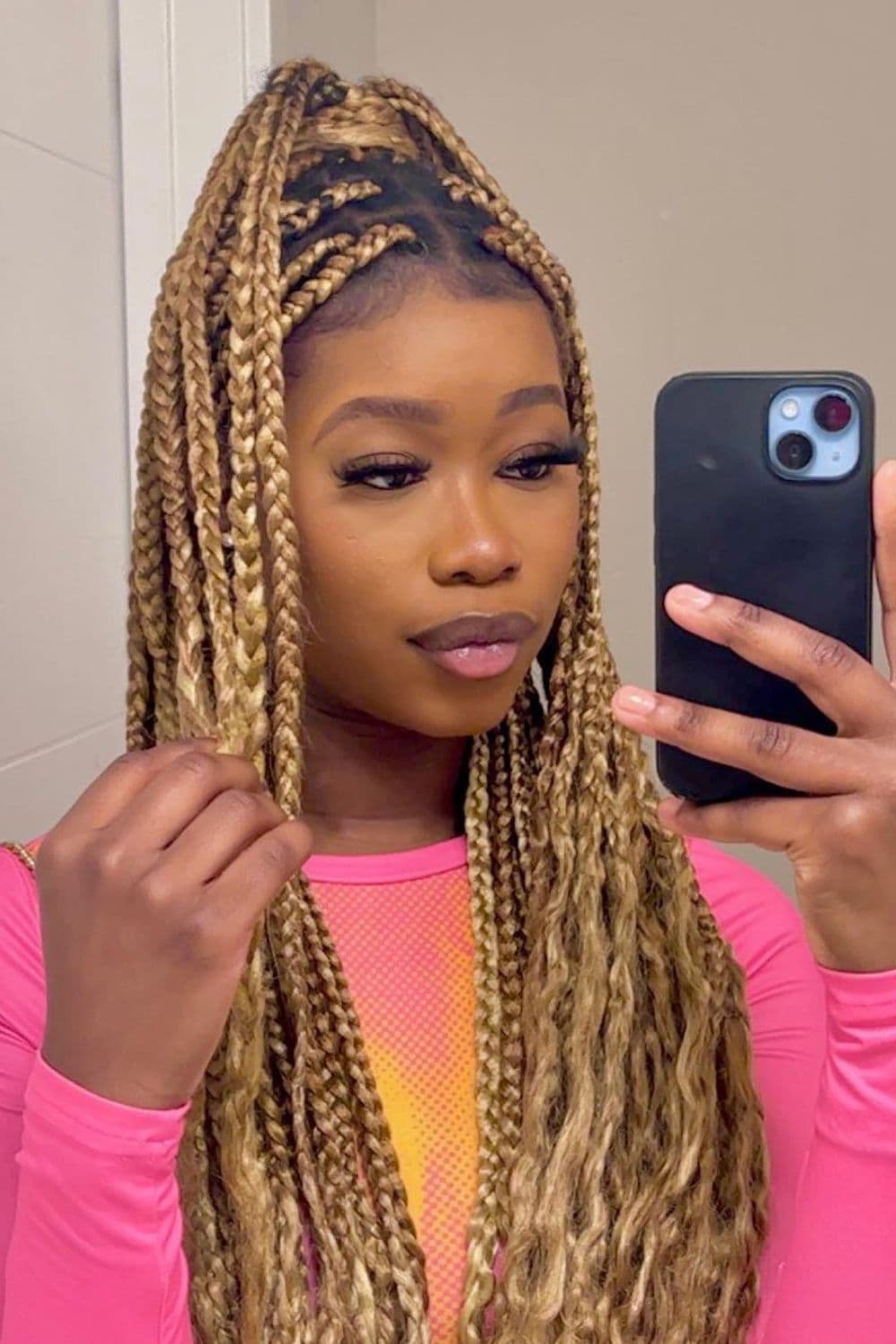 A woman in a pink long sleeve with blonde, half up half down boxed braids with curly ends.