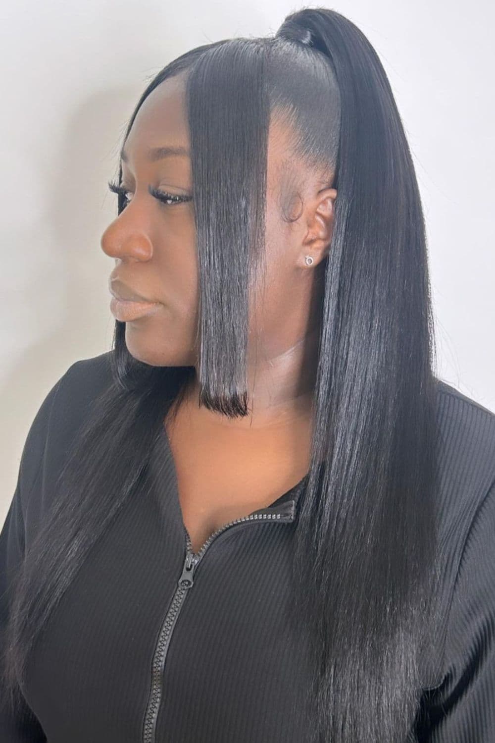 Side view of a woman in a black long sleeve with half up half down with bangs hairstyle.
