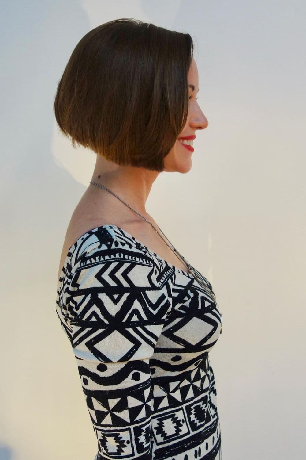 Side view of a woman wearing a black and white patterned blouse with a short A-line cut.