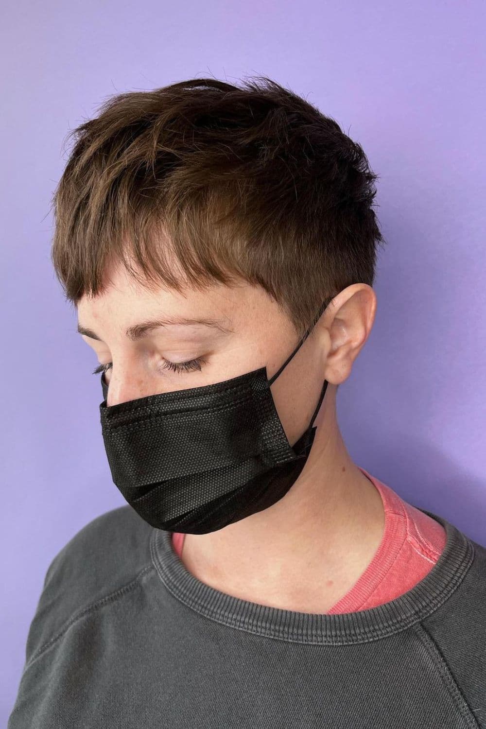 A woman wearing a black surgical mask with a tousled pixie cut.