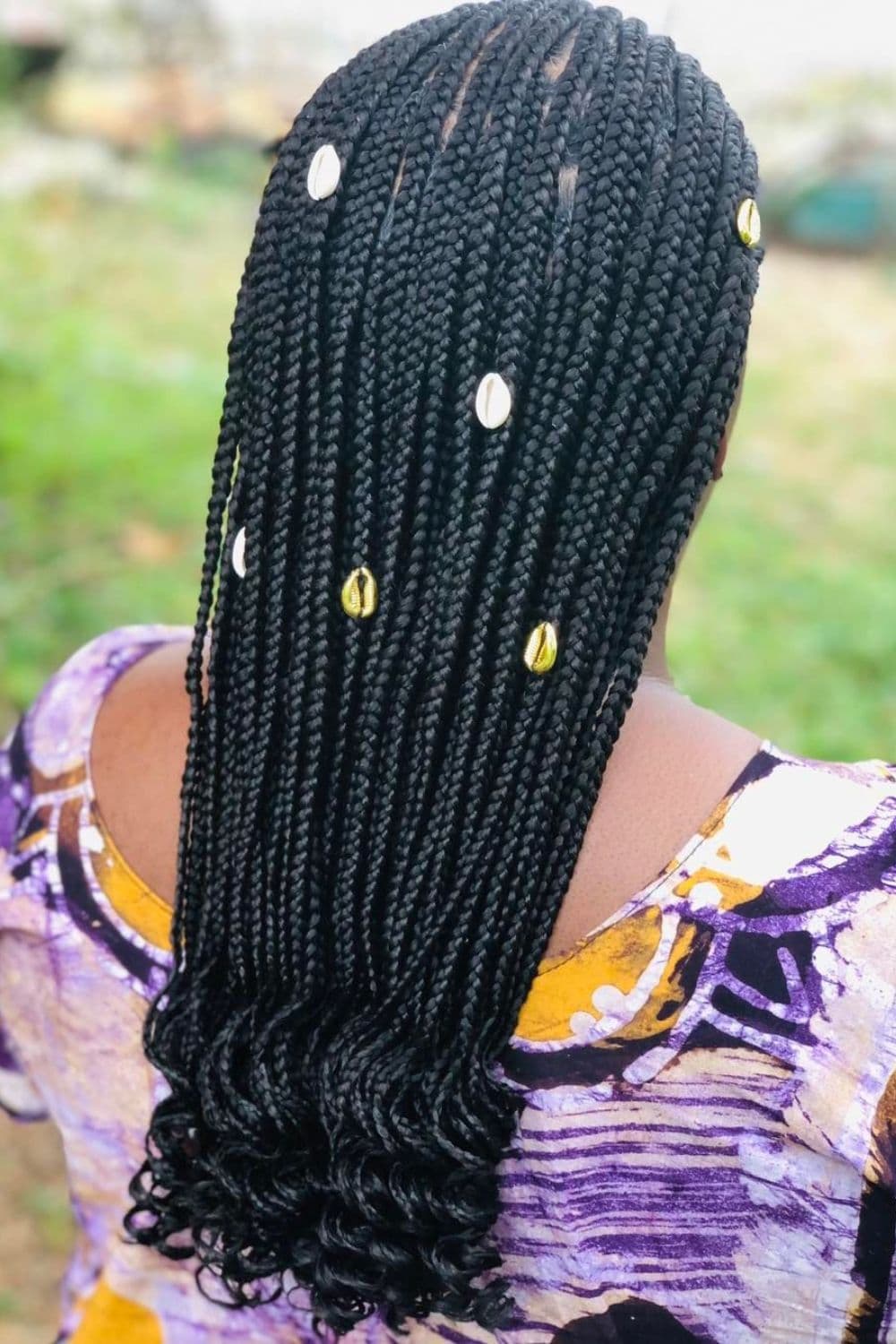 Back of a woman with black medium knotless braids with shell accessories and curly ends.