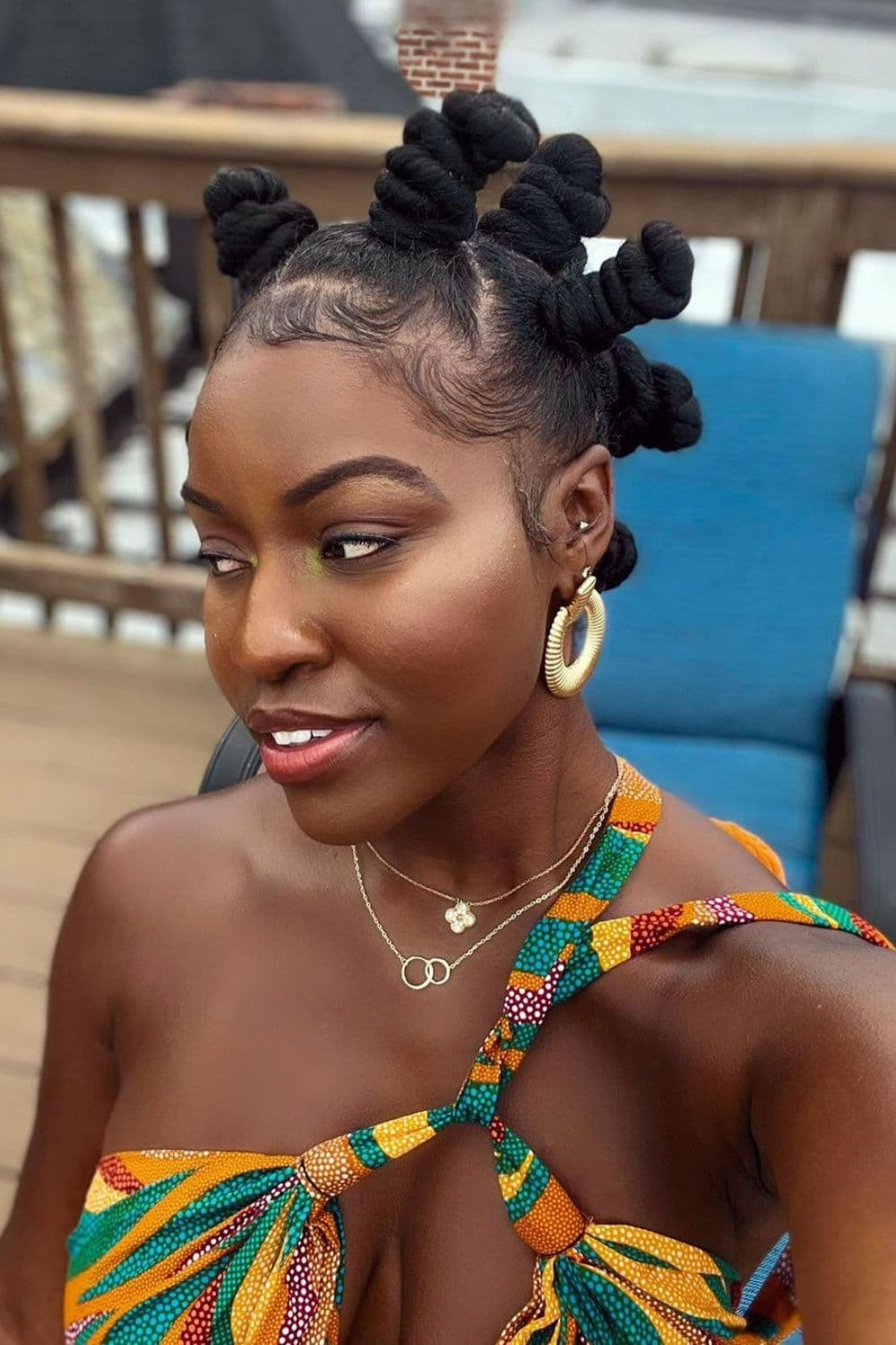 A woman wearing gold earrings and a gold necklace with Bantu knots.