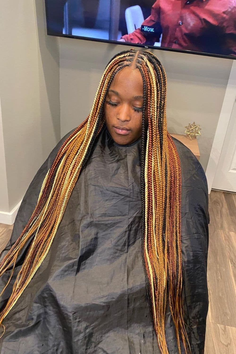 A woman sitting in a salon with black, brown and blonde knotless braids.
