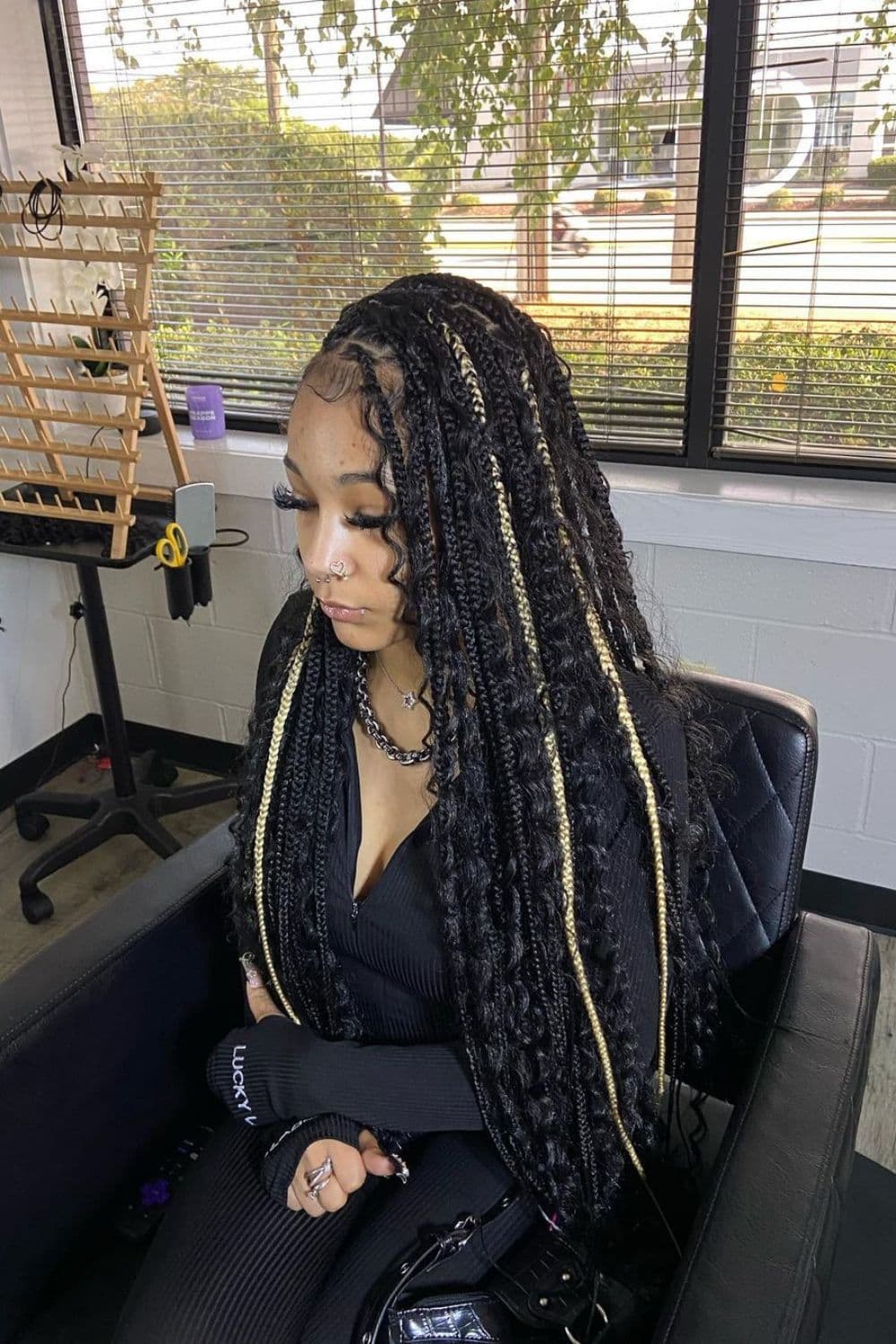 A woman sitting with black goddess braids with blonde highlights.