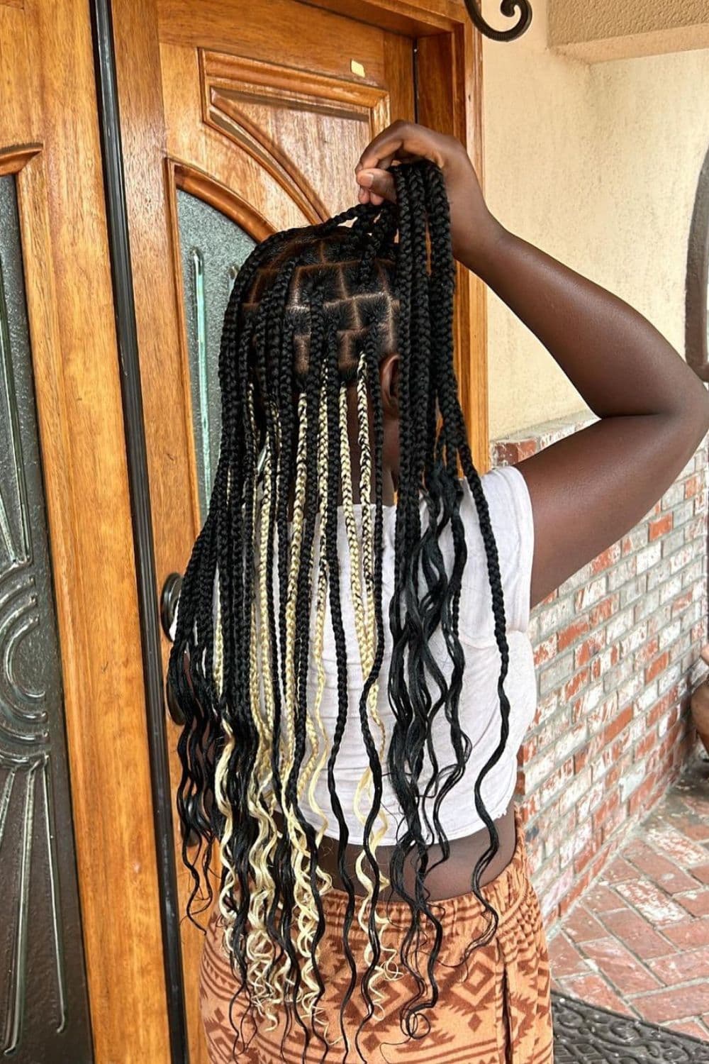 A woman with a black and blonde peekaboo braids is holding her hair.