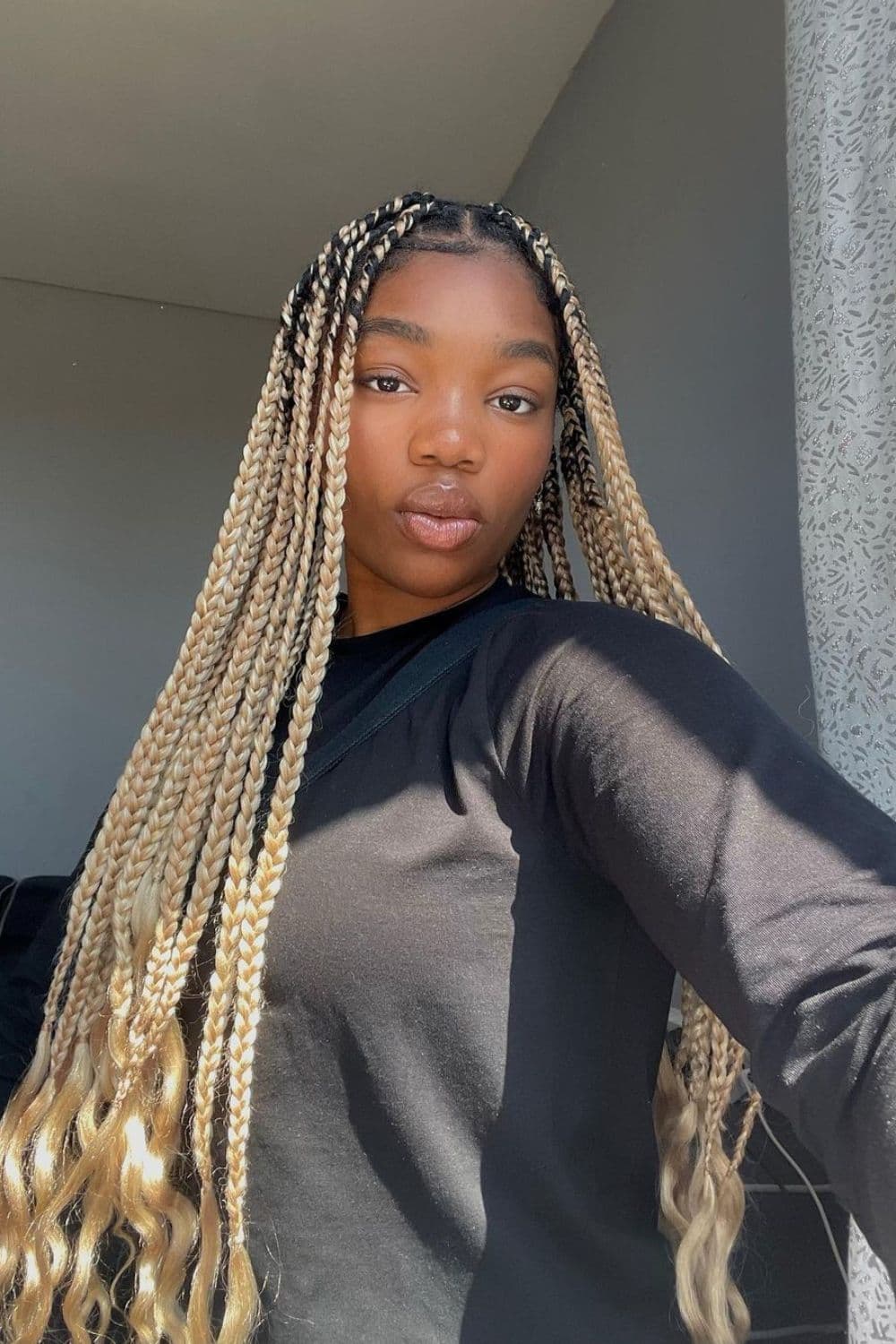 A woman in black long sleeves with blonde medium box braids.