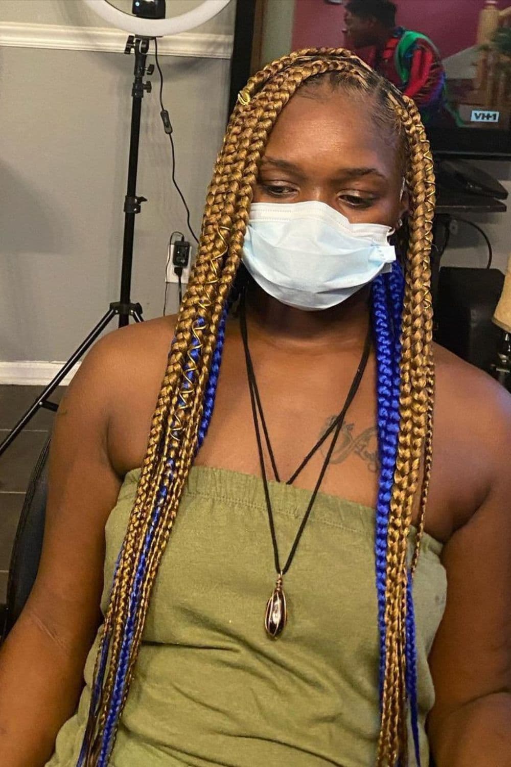A woman with blonde and blue knotless braids is wearing a surgical mask.