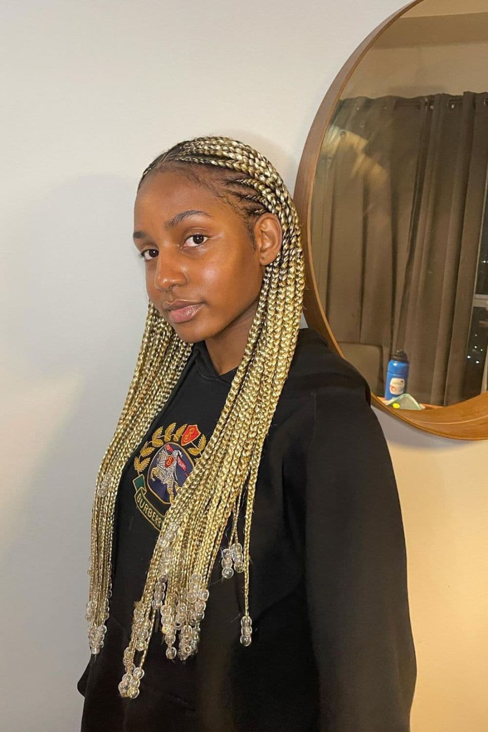 A woman wearing a black sweater with blonde cornrows with beads.