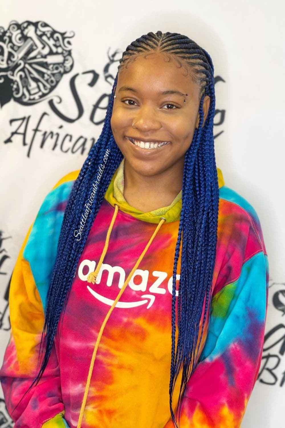 A woman in a colorful sweater with blue middle-parted tribal braids.