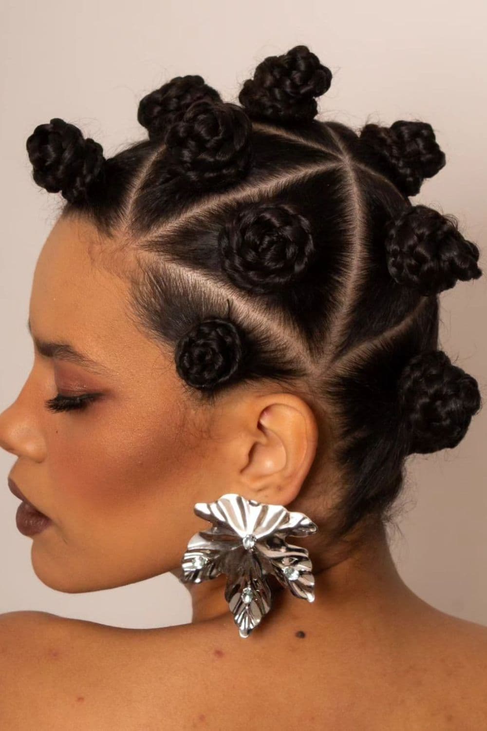Side view of a woman wearing a silver leaf earring with box braids into Bantu knots.