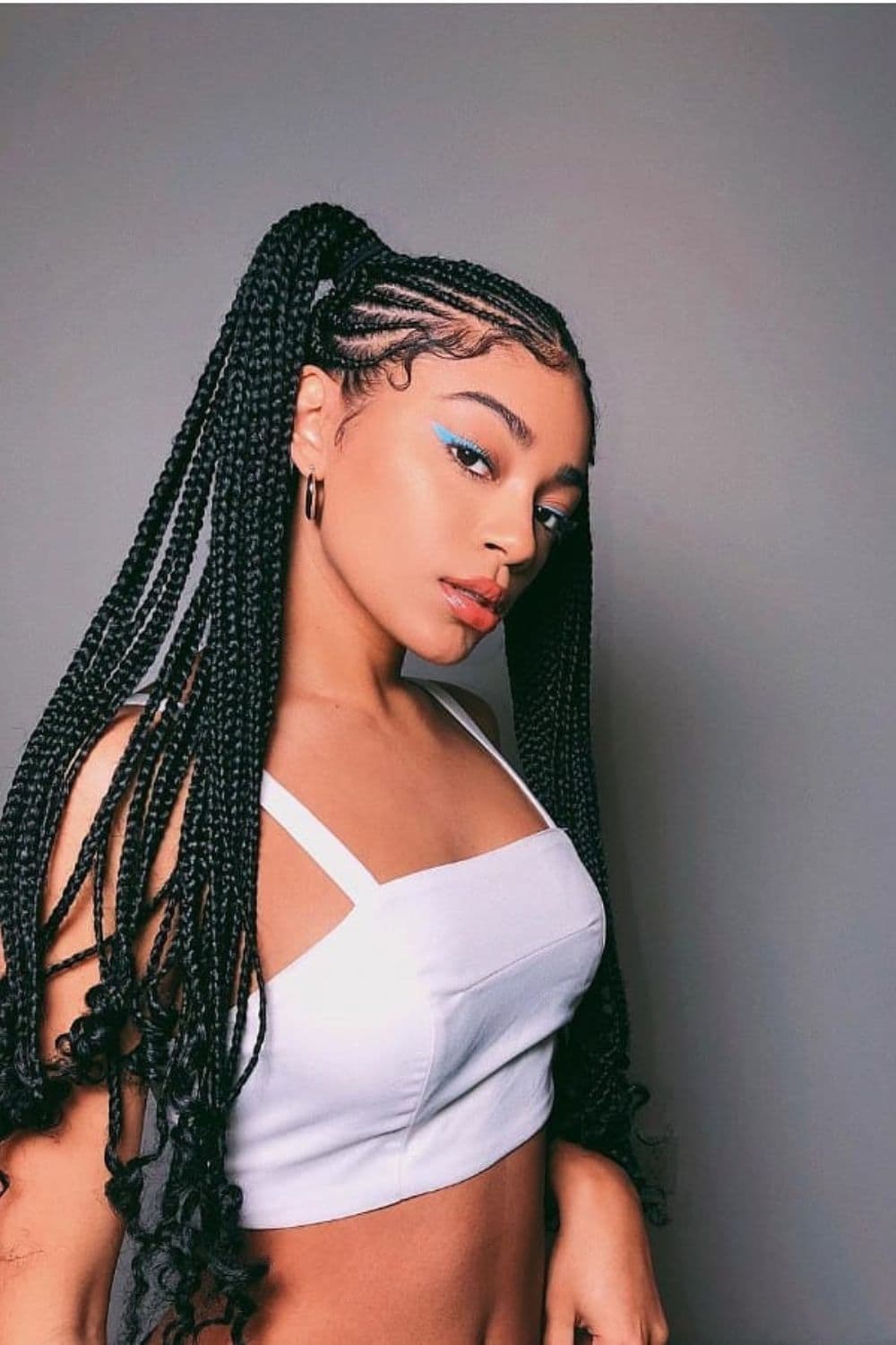 Side view of a woman with a white sleeveless crop top with black box braids with pig tails with curly ends.