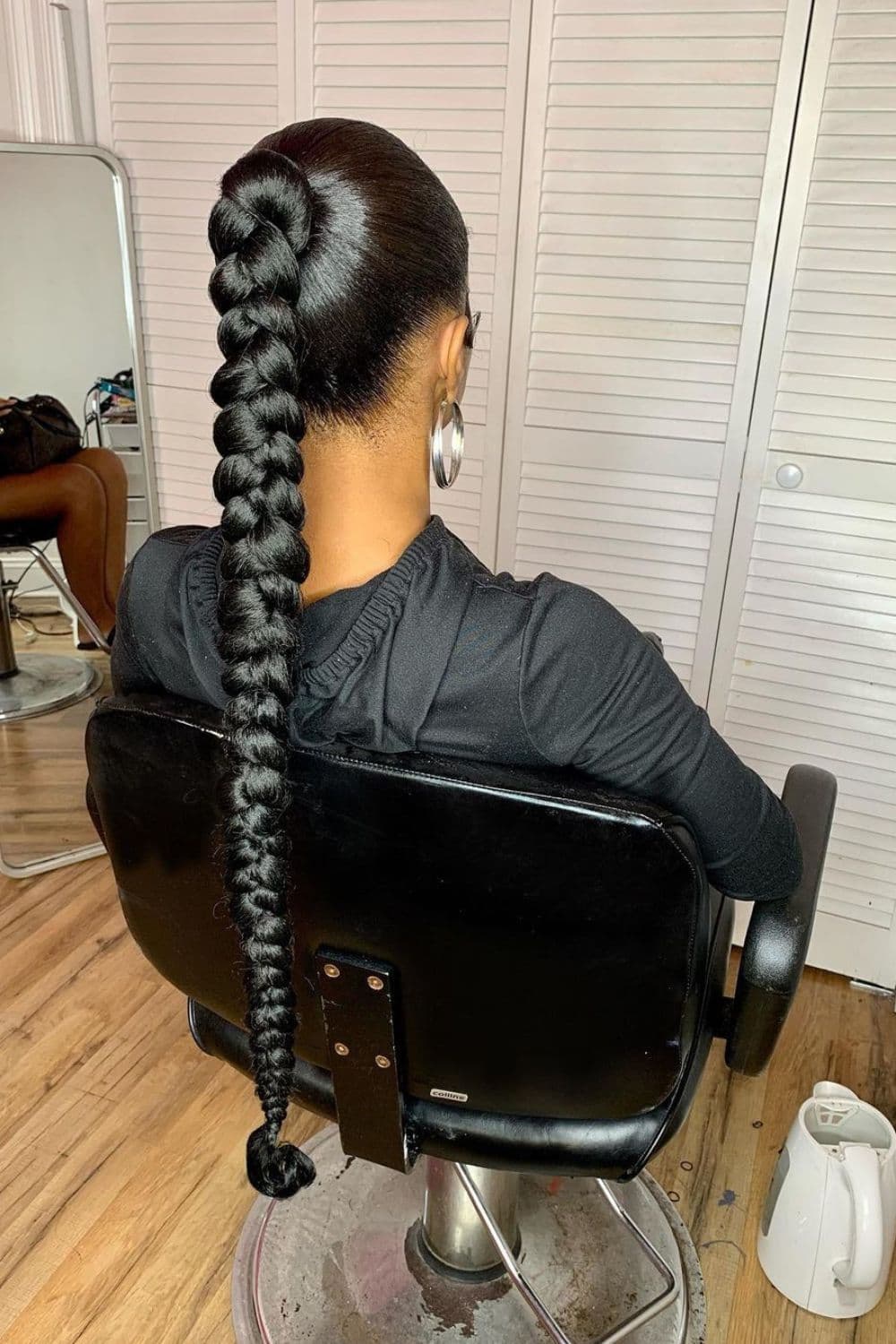 A woman sitting on a swivel chair with a black braided ponytail.