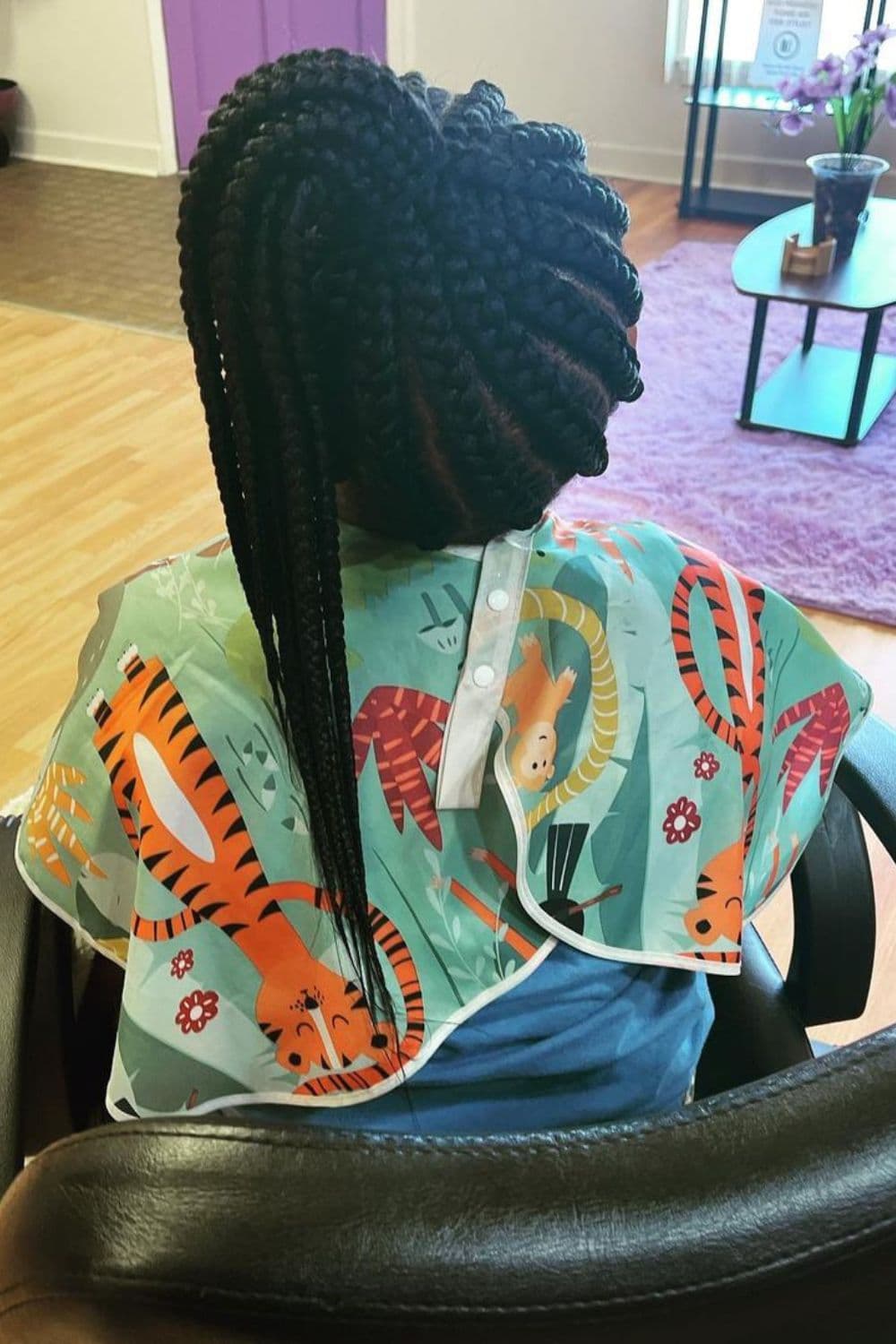 A girl sitting on a chair with a black braided side ponytail.