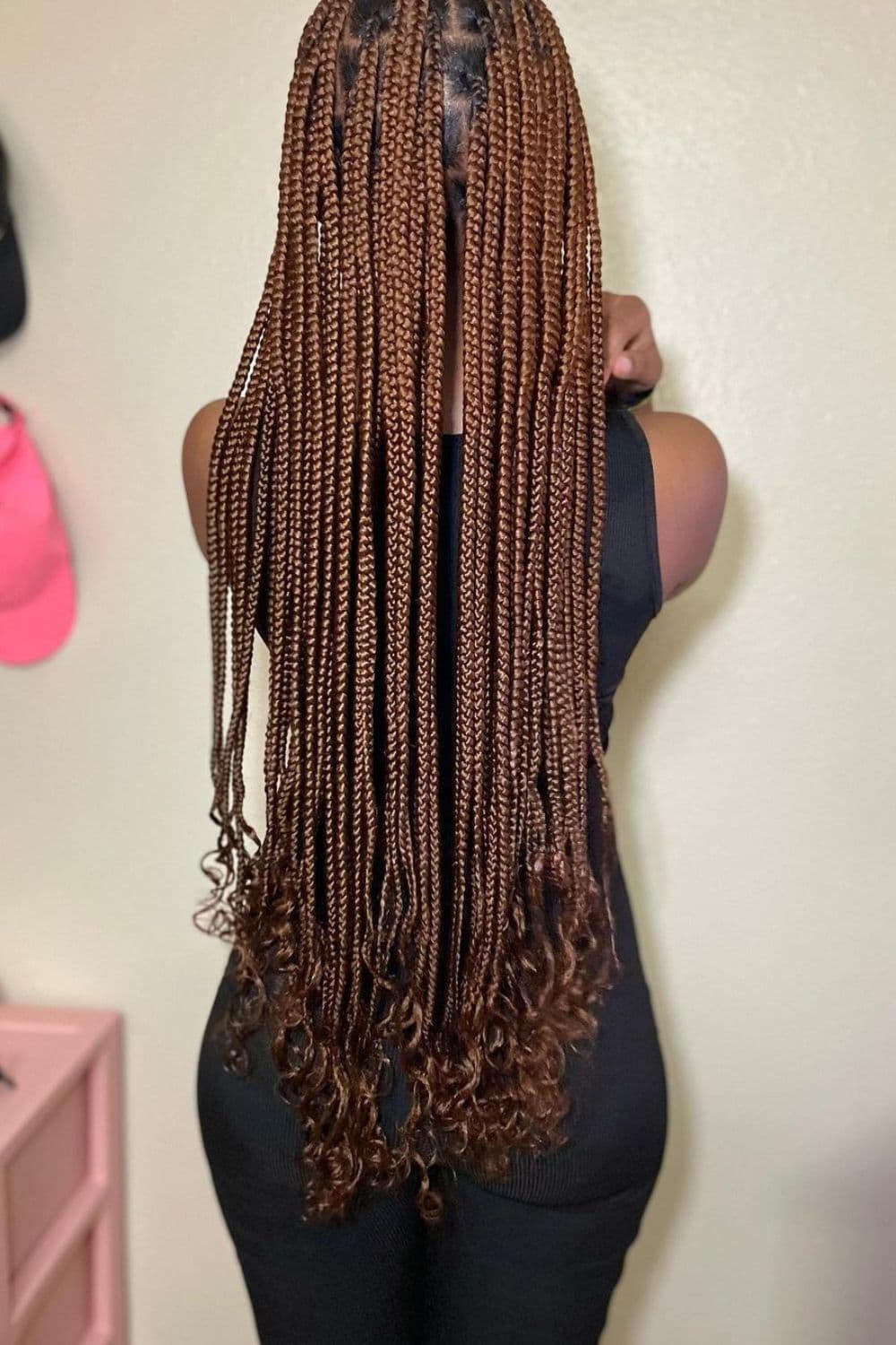 Back of a woman with brown knotless braids with curly ends.