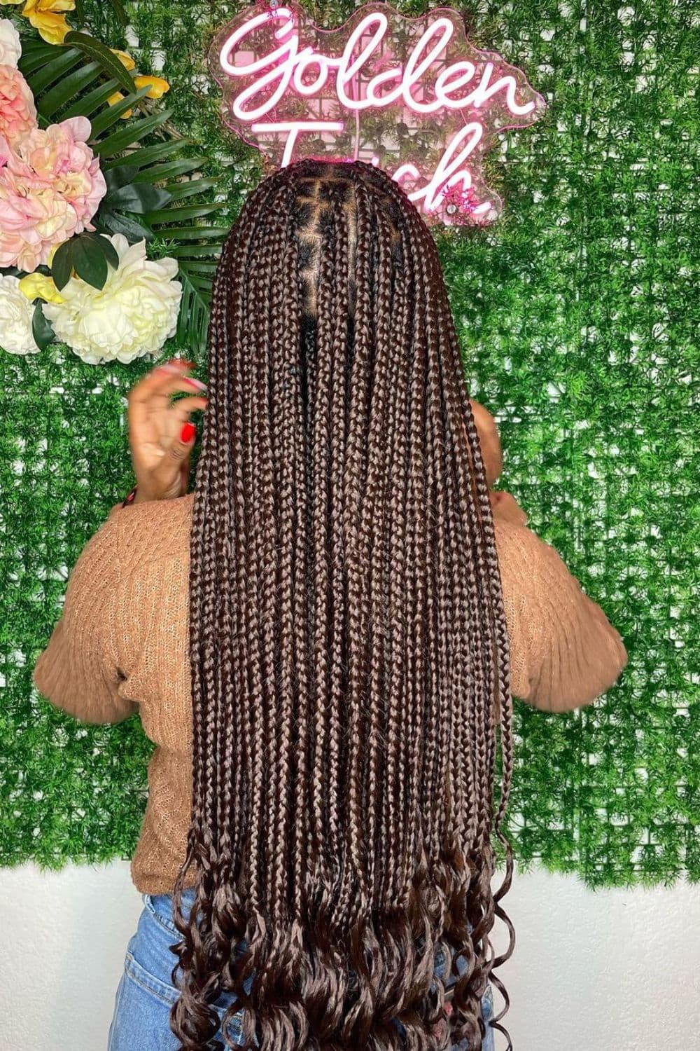 Back of a woman with brown medium knotless braids with curly ends.