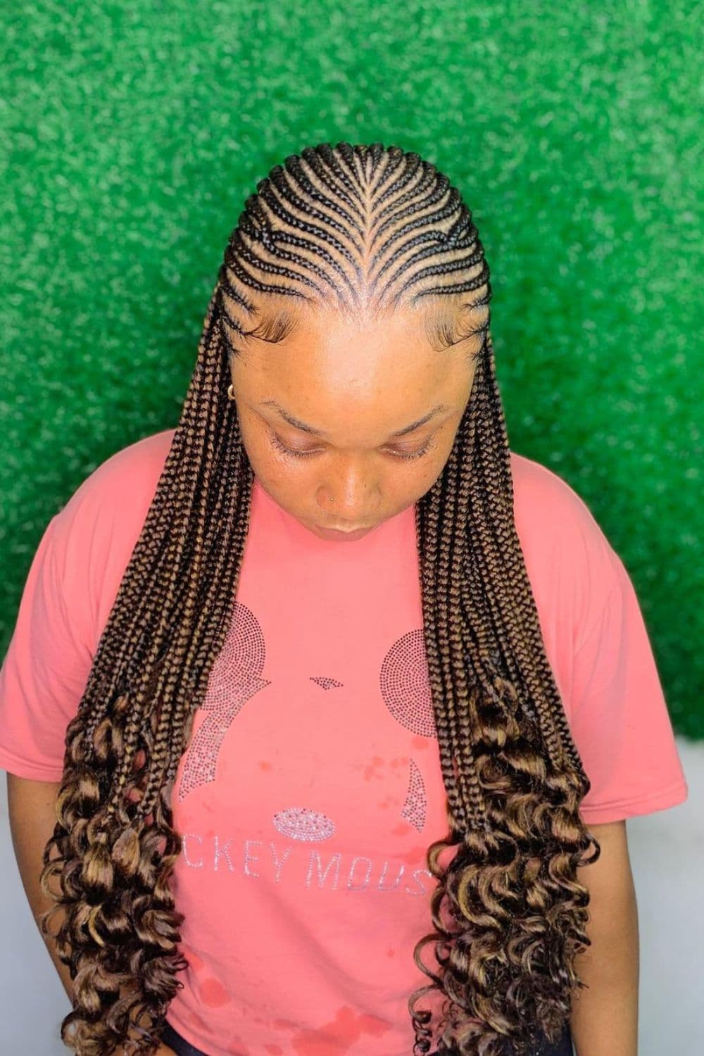 A woman in a pink t-shirt with brown middle-parted tribal braids.