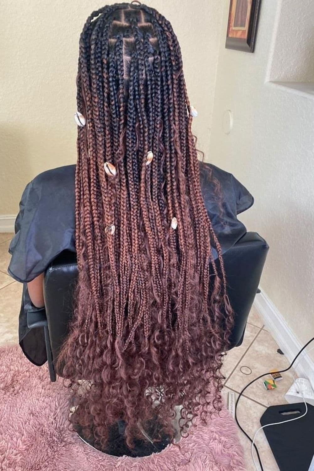 A woman sitting in a hair salon with brown ombre goddess braids with shells.