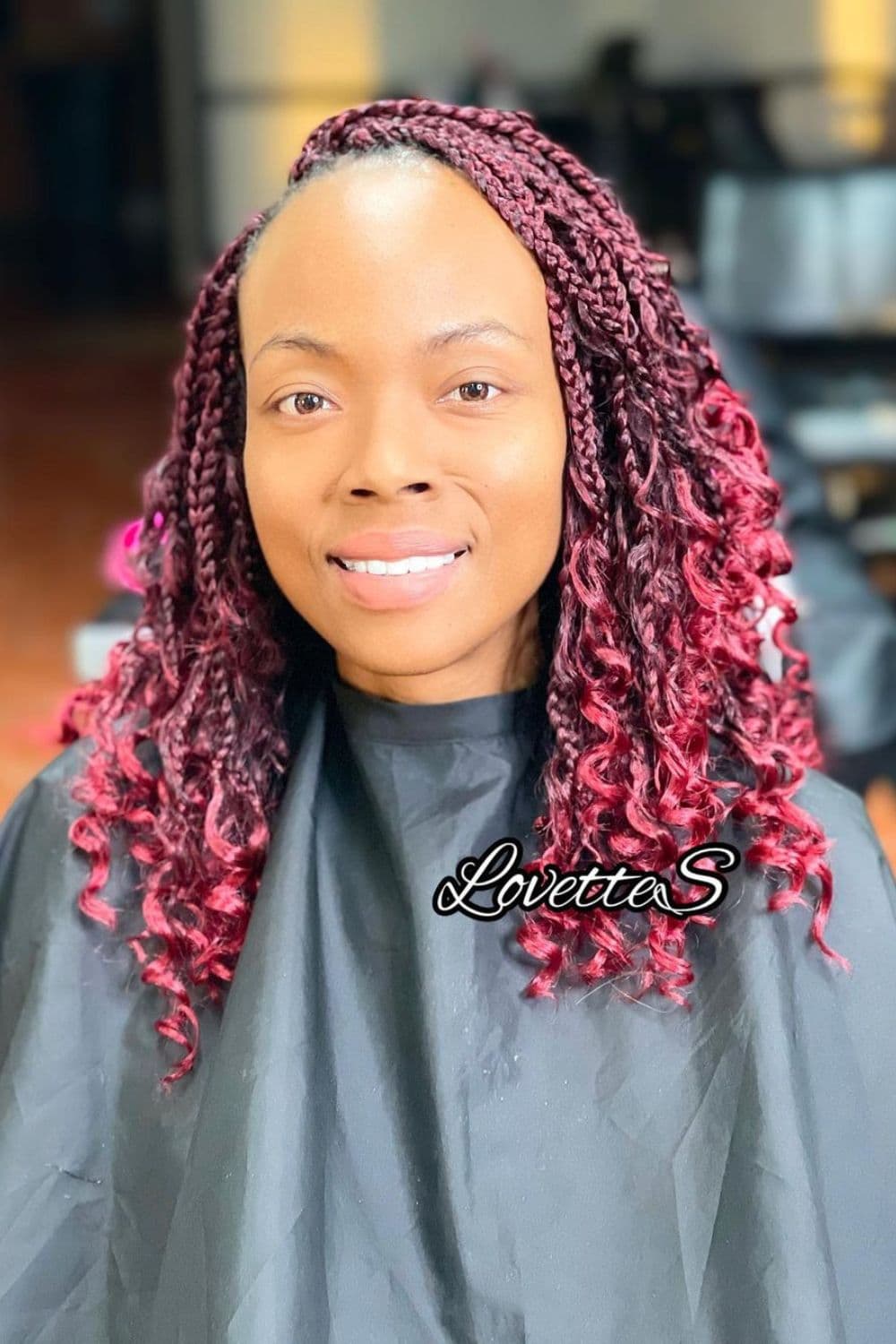A woman with burgundy crochet braids with curly ends.