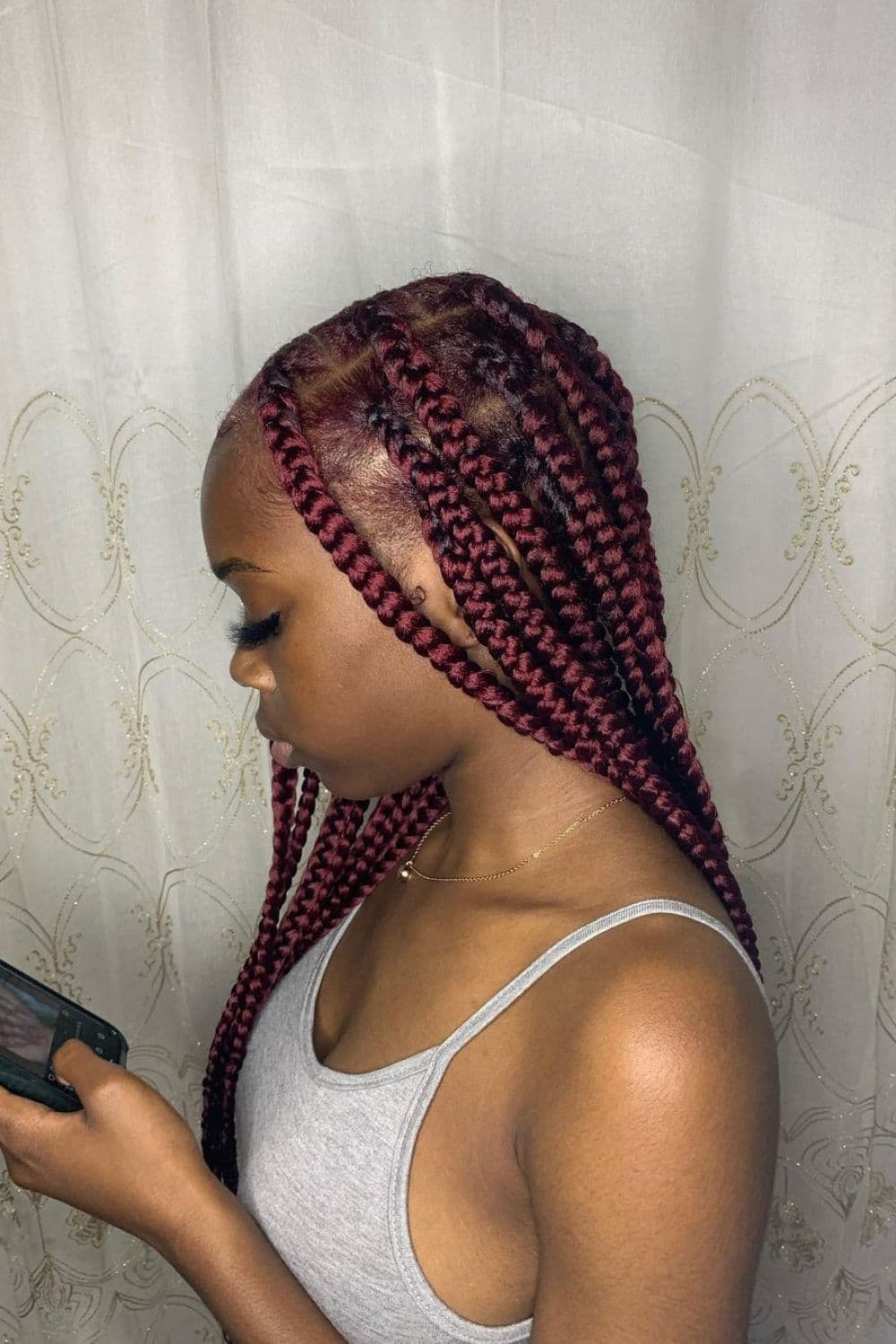 Side view of a woman in grey tank top with burgundy knotless braids.