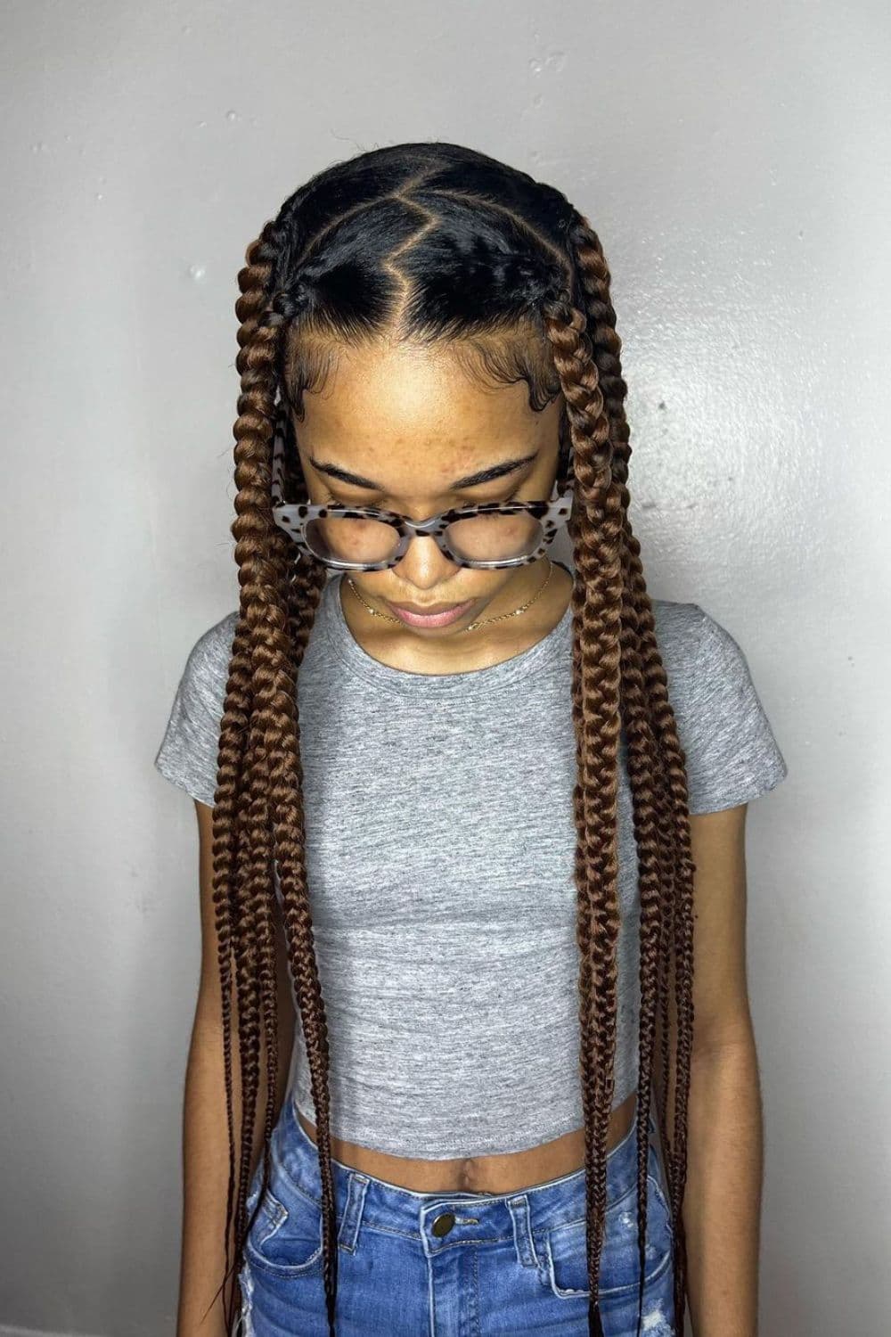 A woman wearing eyeglasses and a grey crop top with brown center-parted knotless braids.