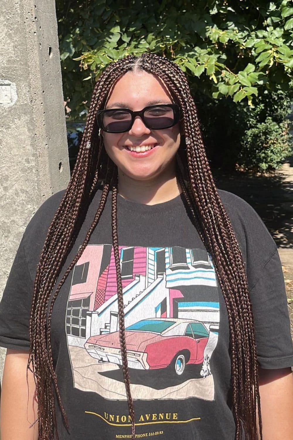 A woman wearing a black t-shirt and sunglasses with black center-parted mini braids.