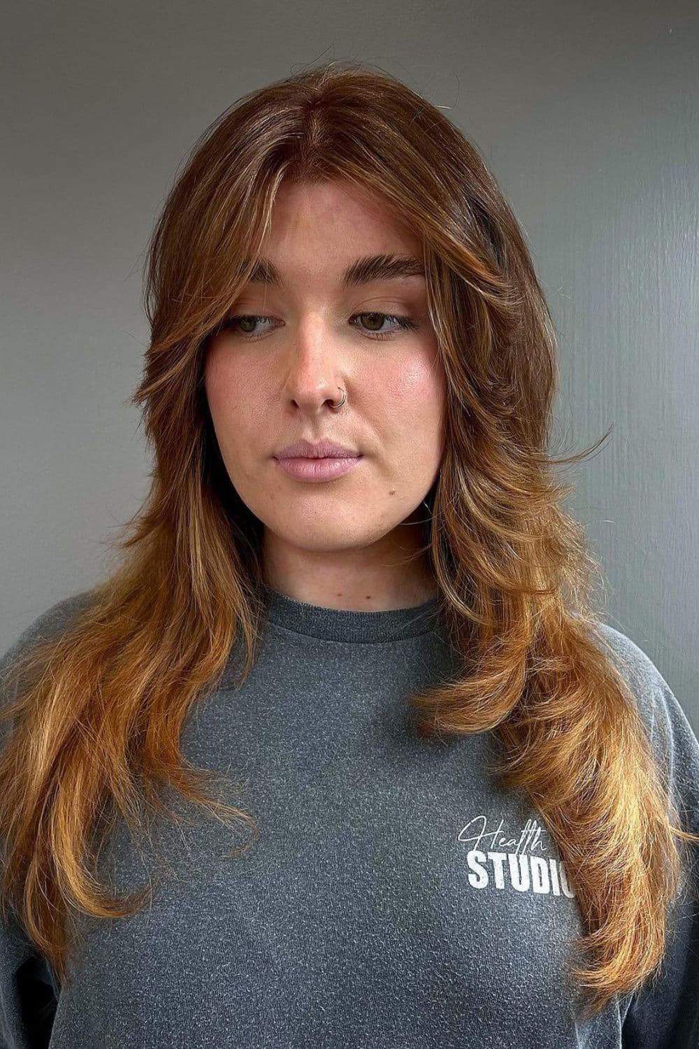 A woman with a long, copper balayage, choppy front layers.