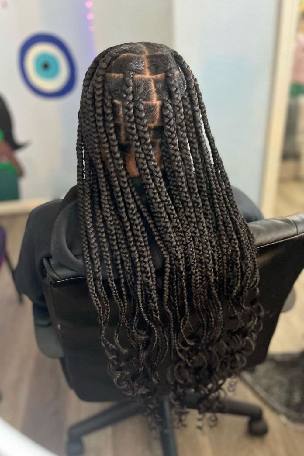 A woman sitting in a salon with classic black medium knotless braids with curly ends.