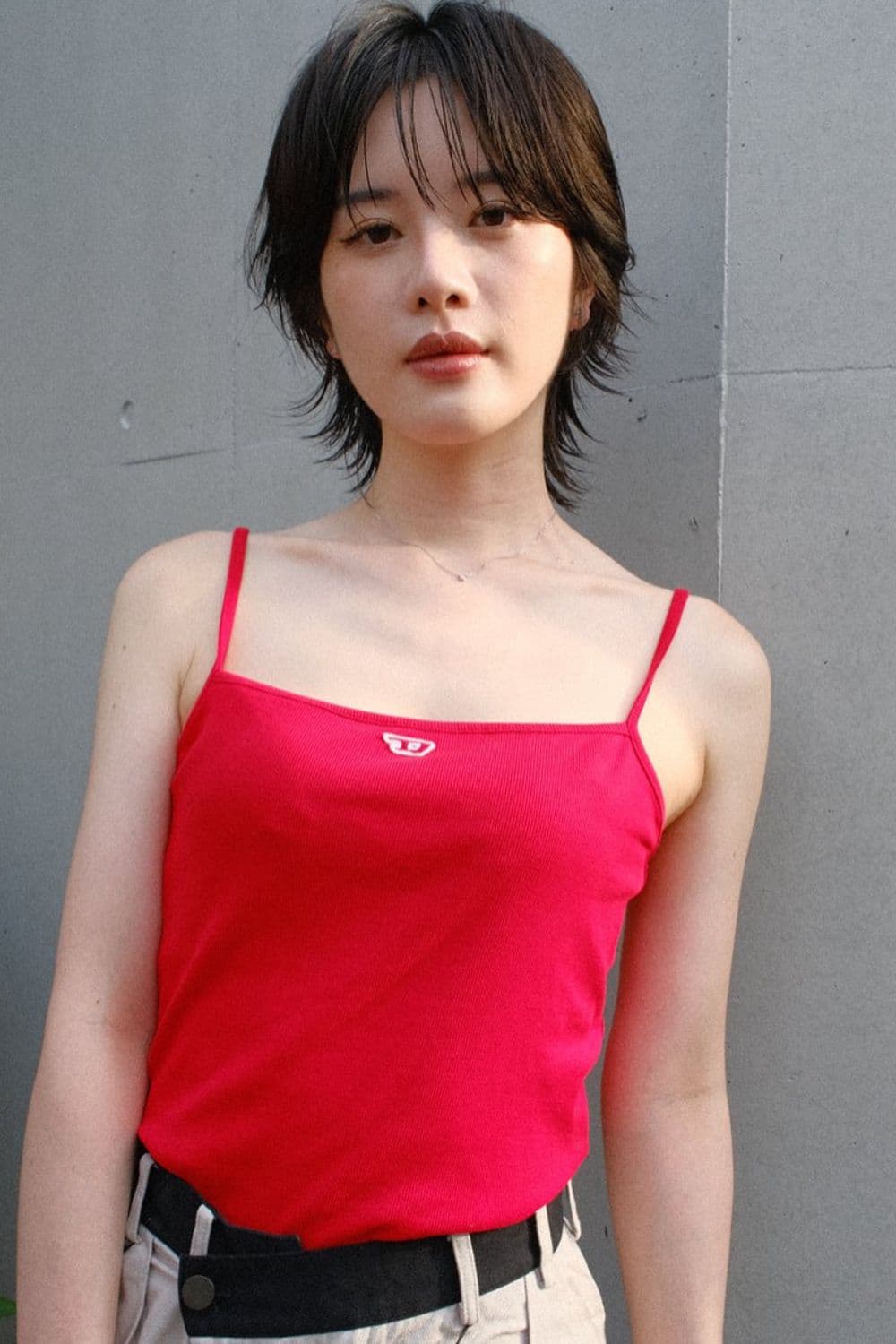 A woman wearing a red tank top with a classic short wolf cut.