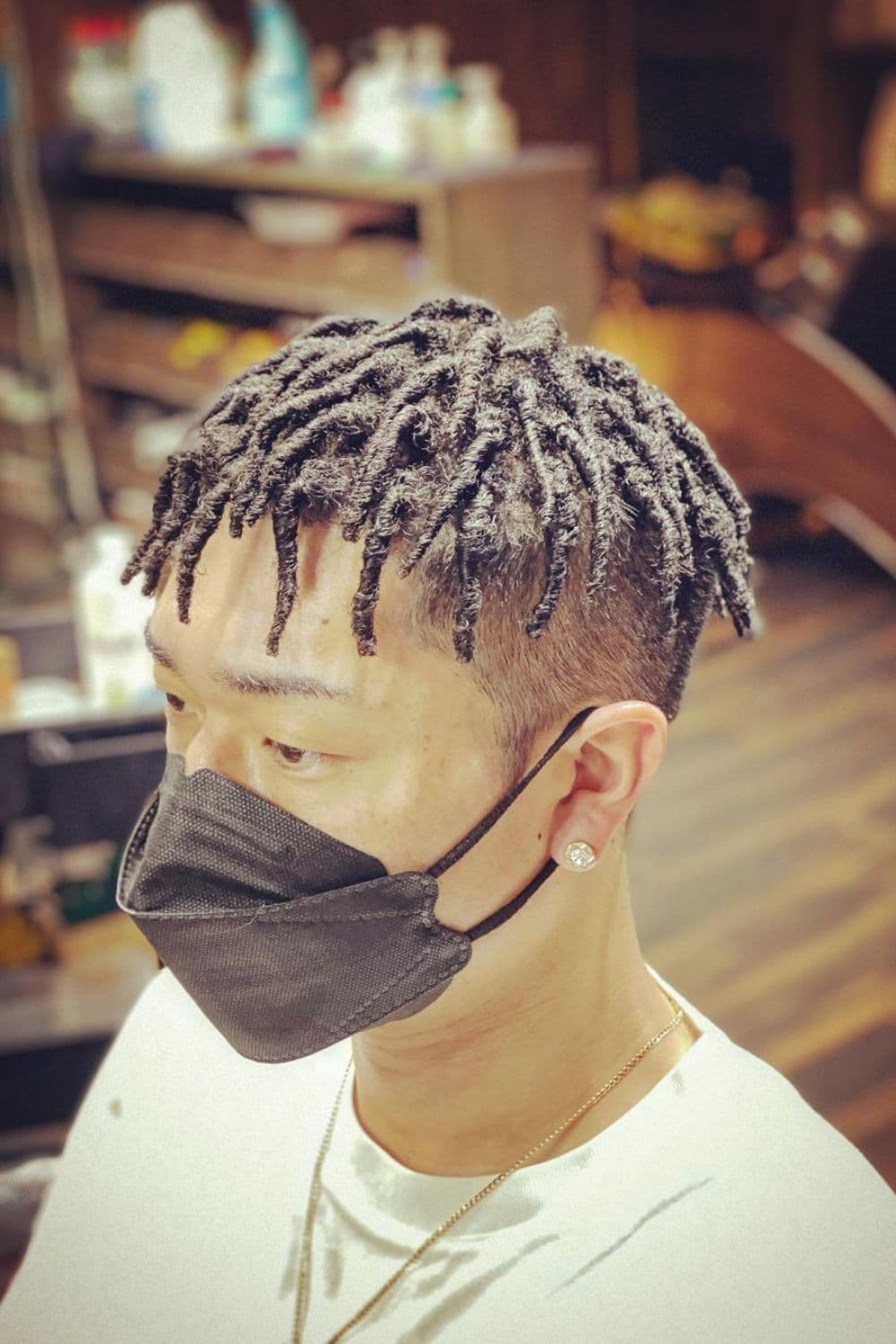 Side view of a man wearing a black surgical mask with a comb twist with undercut.