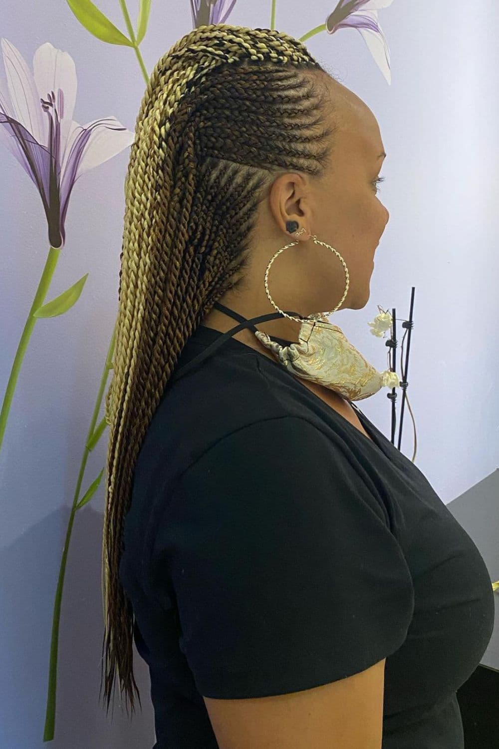 A woman standing with brown and blonde cornrow mohawk.