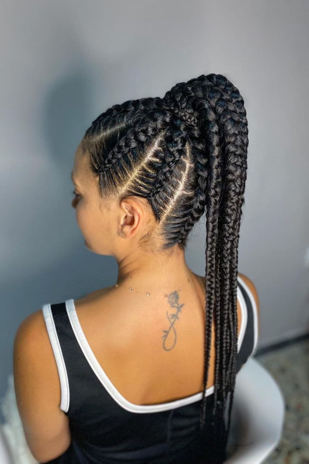 Side view of a woman in a black and white tank top with a black cornrow ponytail.