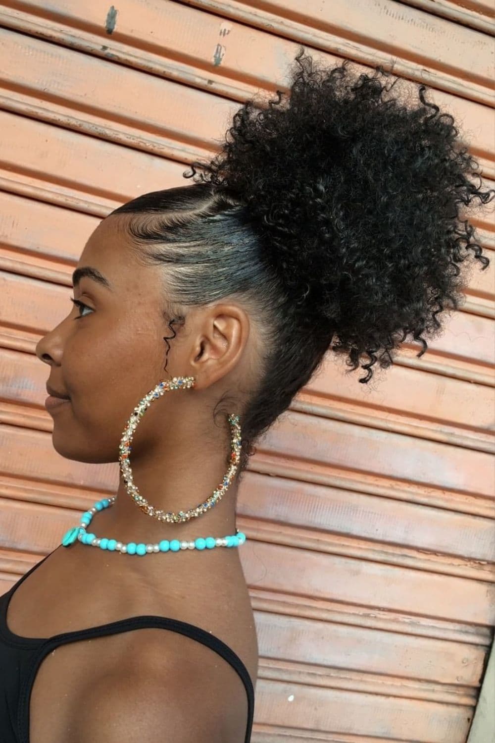 Side view of a woman wearing a big round earring, a beaded necklace, and a black crochet high puff.