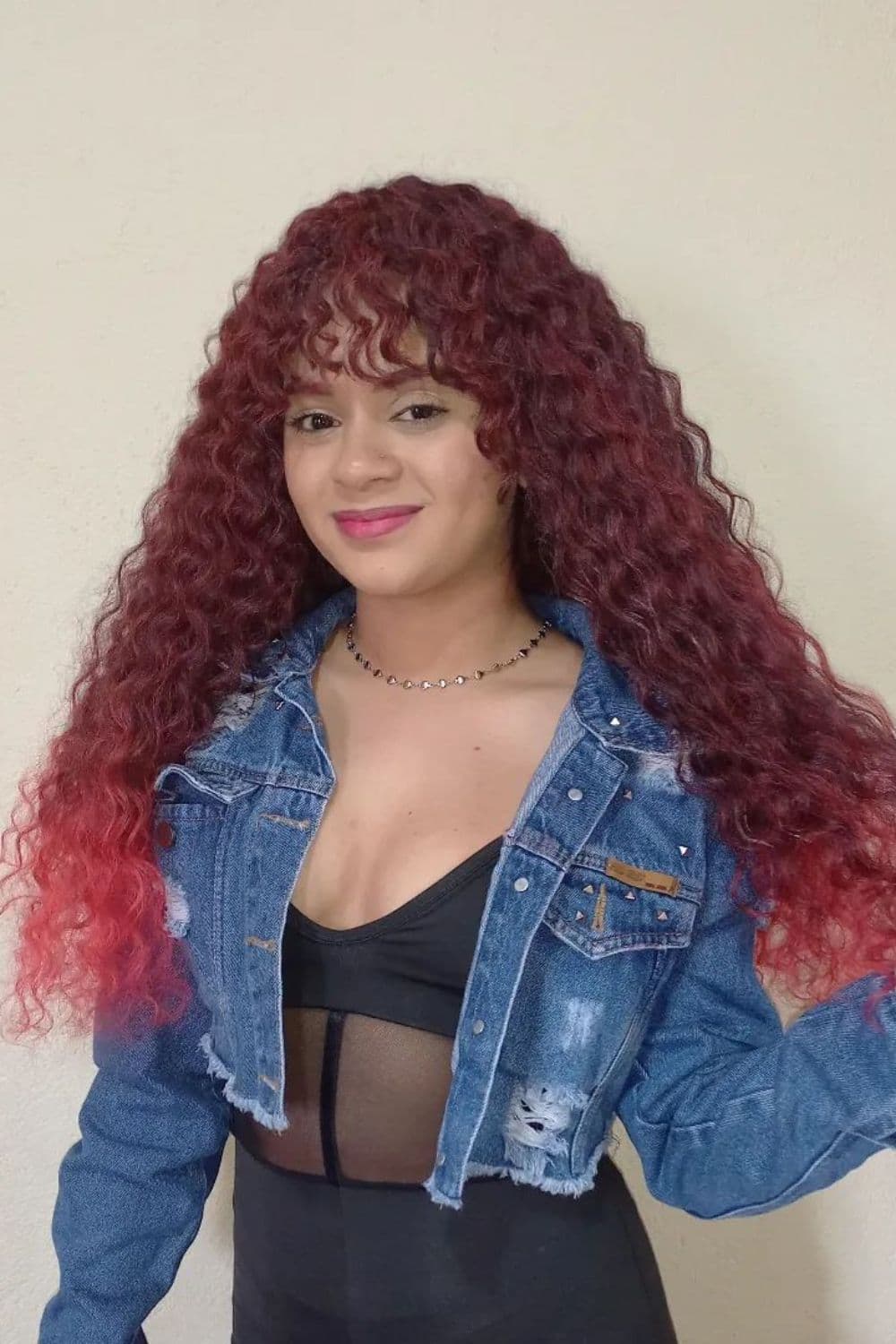 A woman wearing a black tube top, a denim jacket, and, red curly crochet with bangs.