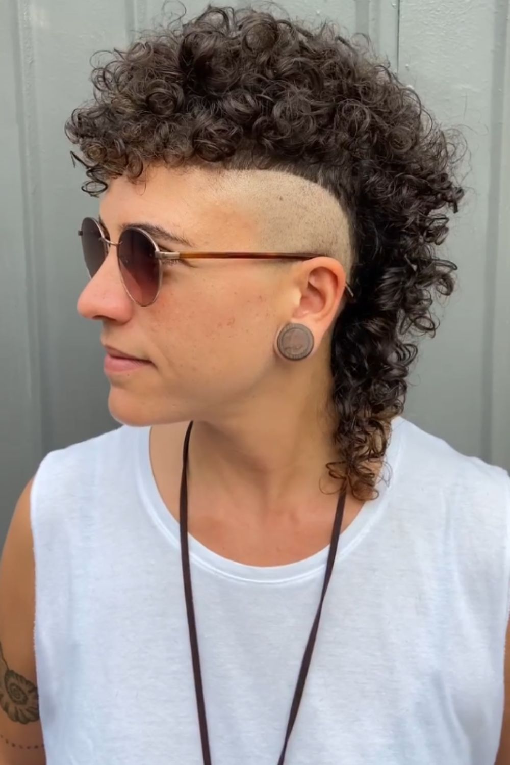 A man wearing sunglasses with curly mullet with bald fade.