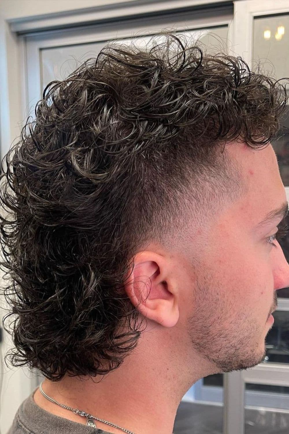 Side view of a man with curly mullet with high fade.