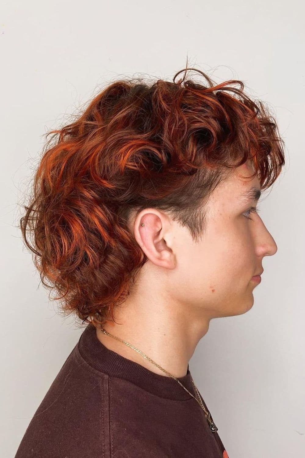 Side view of a man with curly mullet with red highlights.