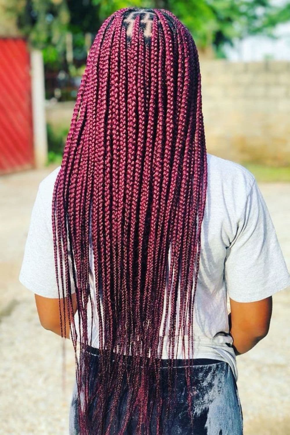 Back of a woman in a white t-shirt with dark maroon knotless braids.