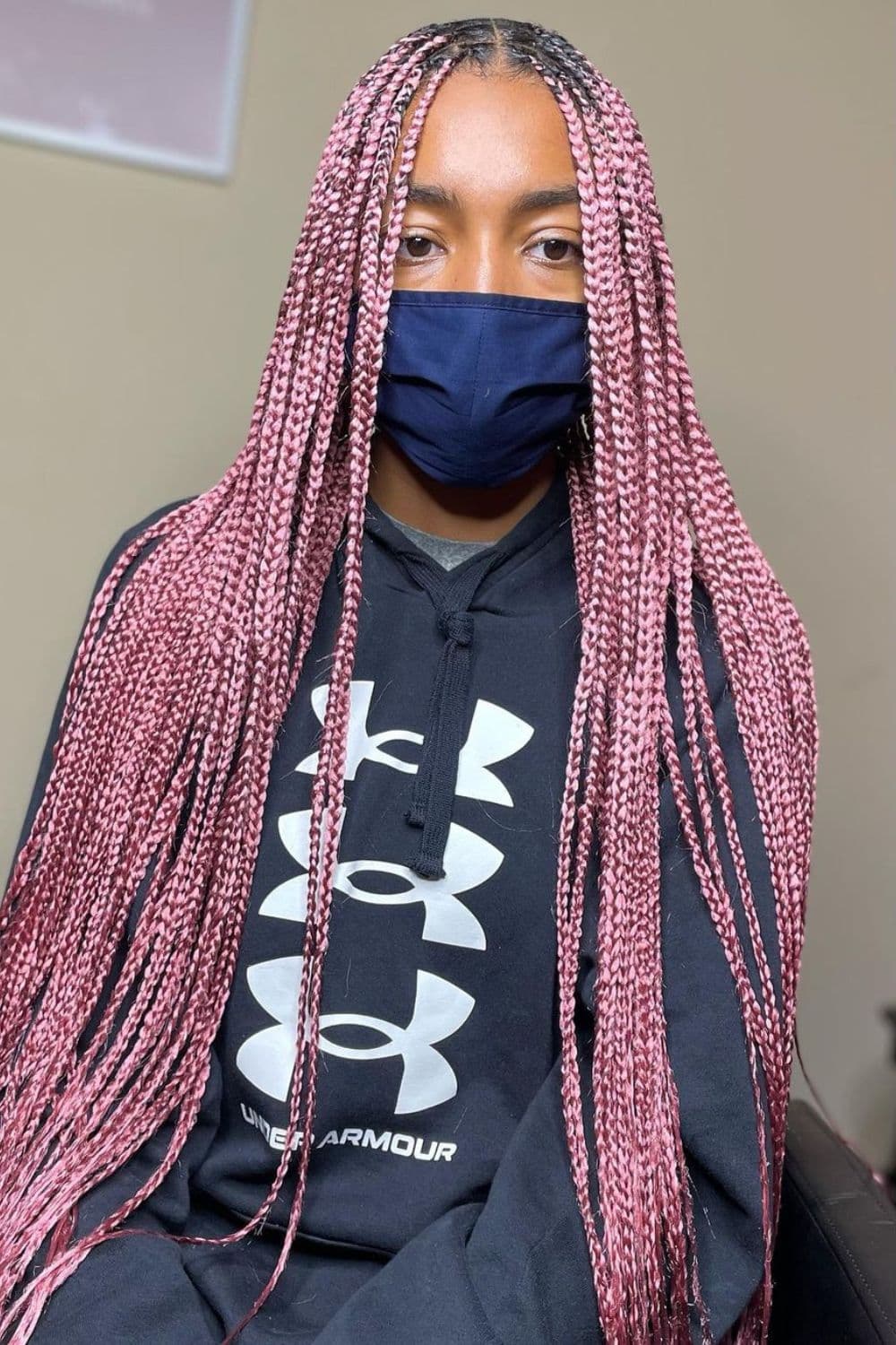 A woman in a black sweater and a black mask with a dark pink knotless braids.