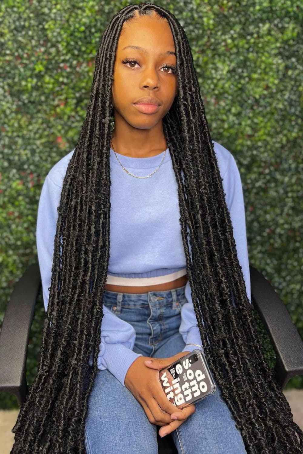 A woman in a blue sweater and jeans with long black faux locs.