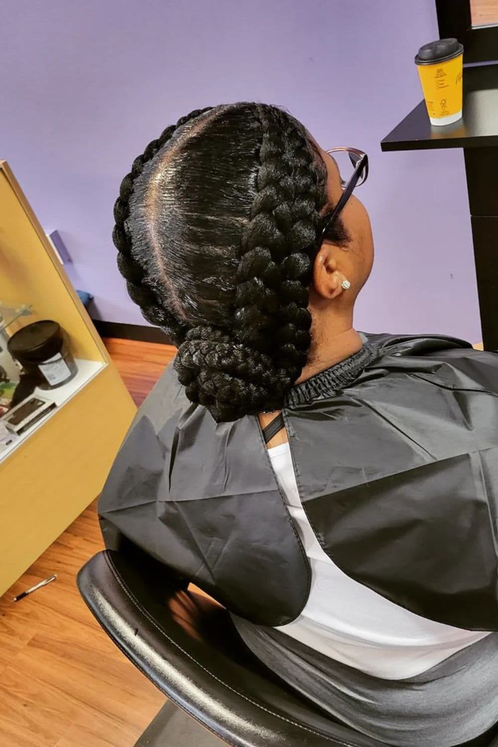 A woman sitting in a salon with four-in-two braids in a low bun.