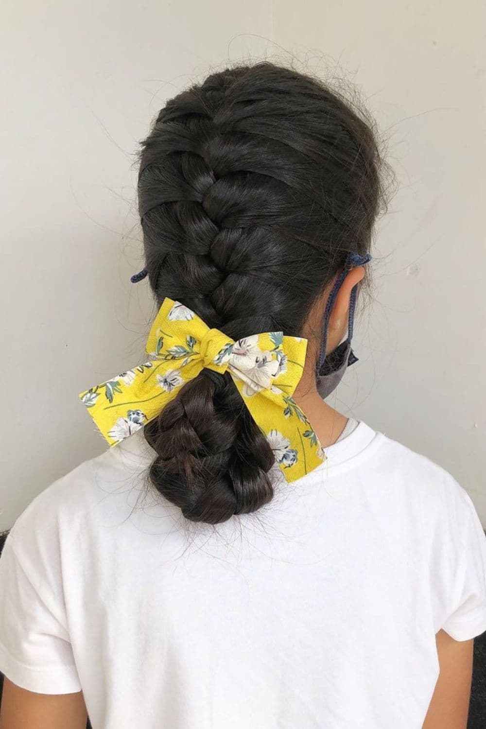 A girl in a white t-shirt with a French braid low bun with yellow ribbon.