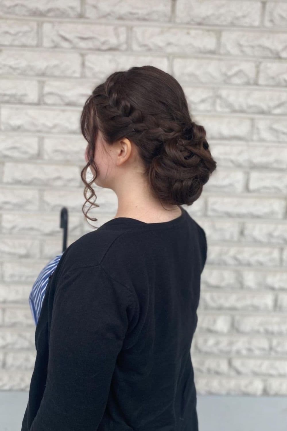 Side view of a woman wearing a black cardigan with a French braid updo.