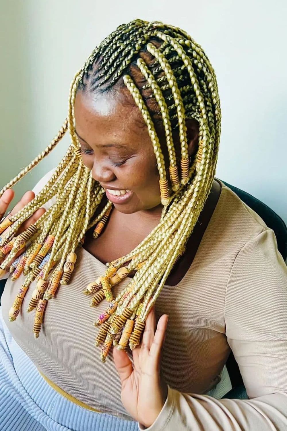 A woman sitting in a salon with blonde Fulani braids with beads.