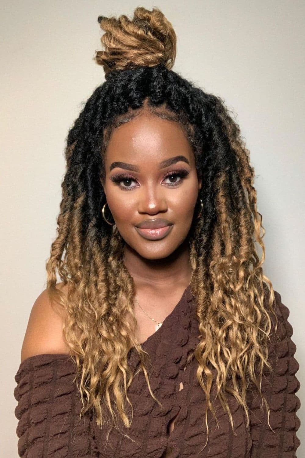 A woman in a brown off-shoulder blouse with half up half down ombre goddess locs.