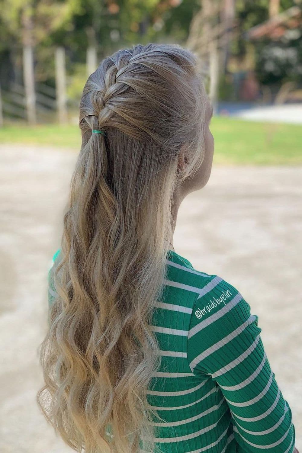 Side view of a woman wearing green and white long sleeves with blonde half-up French braids.