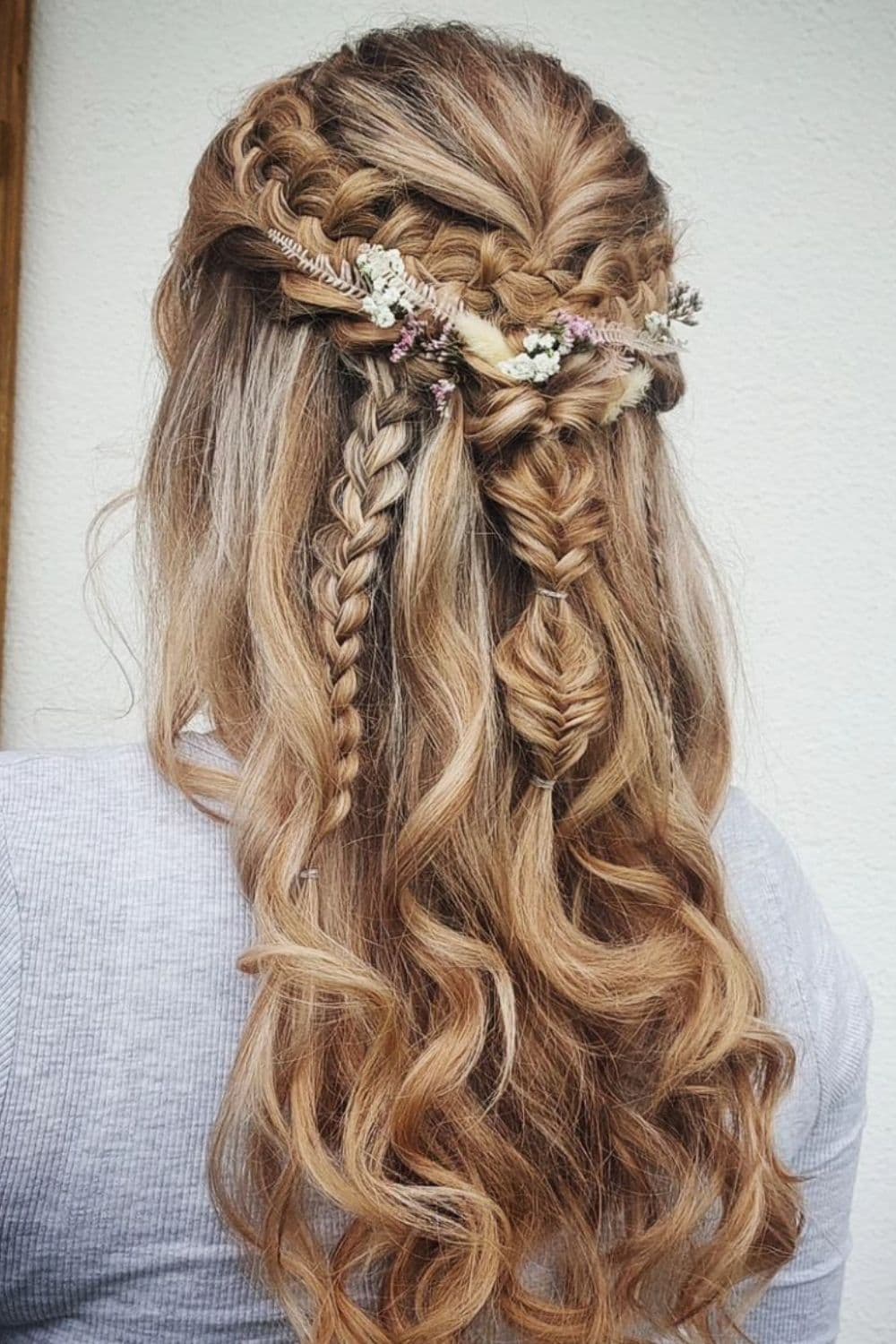 A woman with blonde half up hairstyle with fishtail braids elements and flower hair accessories.