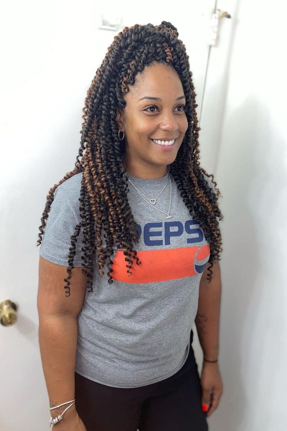 A woman wearing a gray t-shirt with black and brown half-up half-down passion twists.