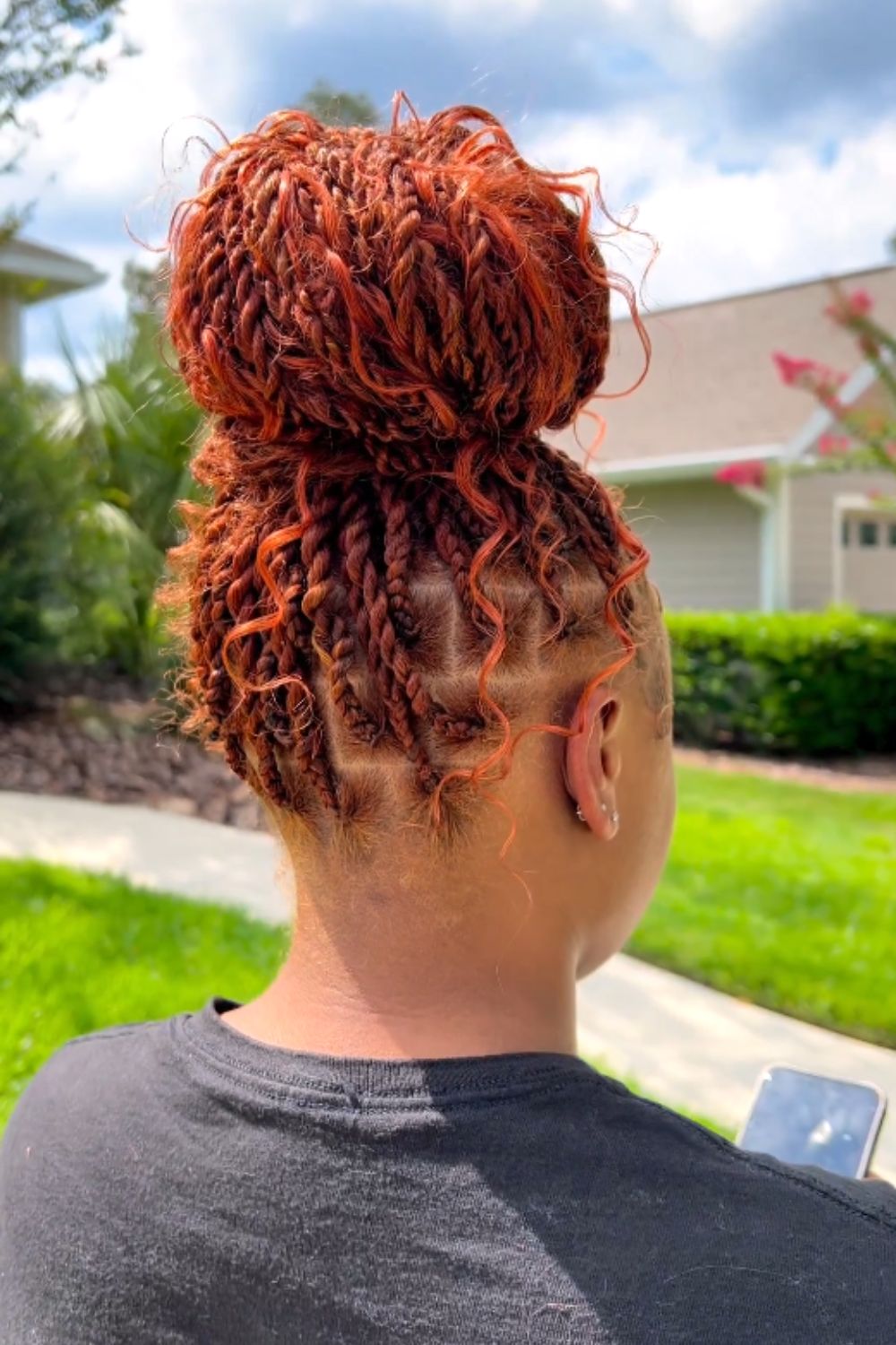 A woman with orange high bun medium knotless braids with curly ends.