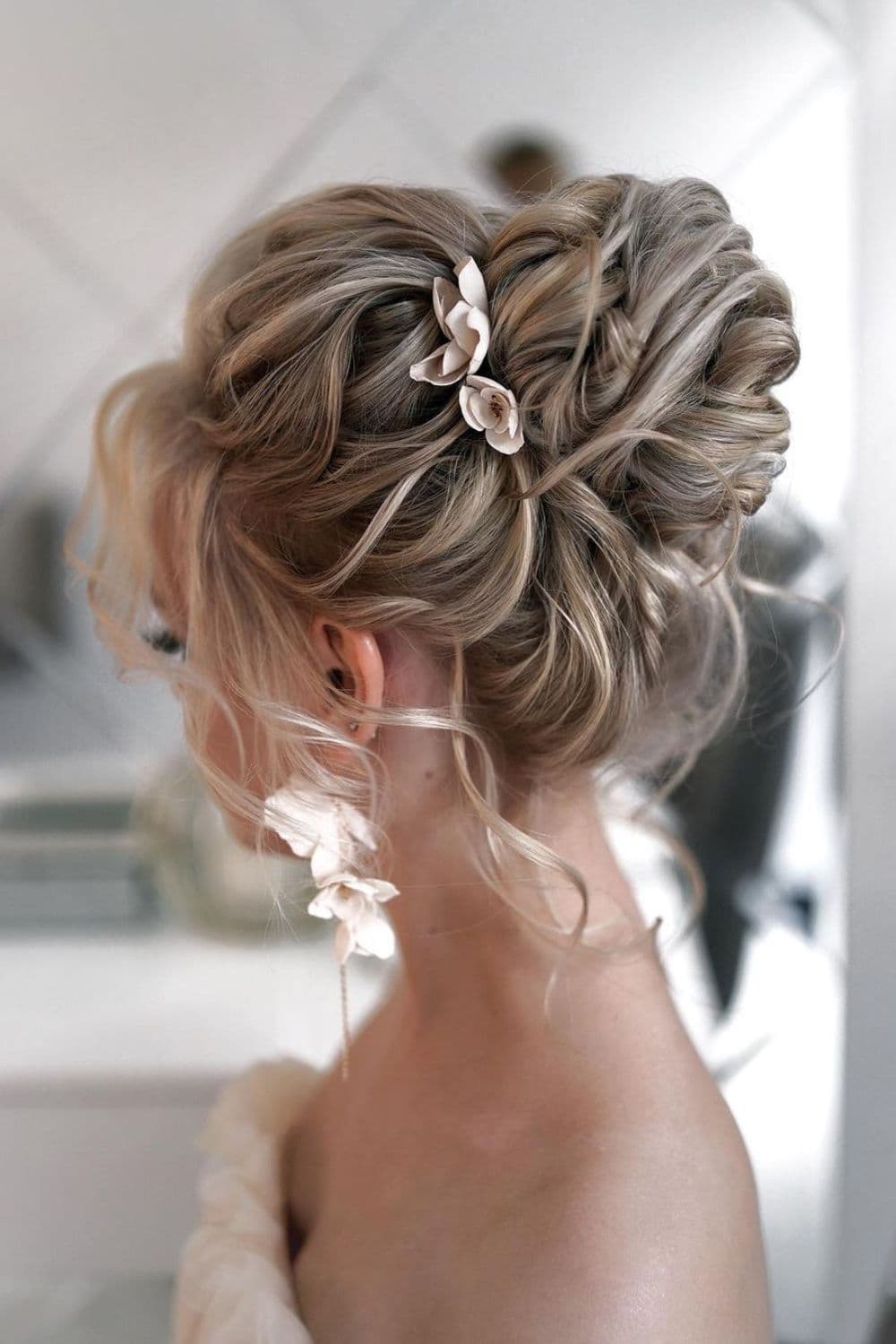 Side view of a woman with a blonde high bun with flowers accessories.